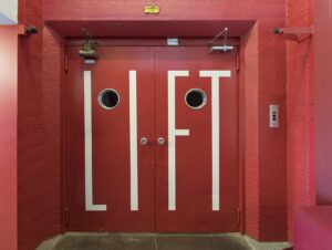 Rode liftdeuren met het woord "LIFT" in witte letters in een felrode hal in de Generaal Vetterstraat.